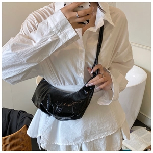 Close-up of a black glossy pleated dumpling bag worn with a white oversized shirt