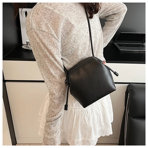 Close-up of black litchi pattern leather texture on a minimalist drawstring crossbody bag