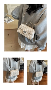 Detail of white quilted crossbody bag featuring a silver chain strap and metal turn-lock