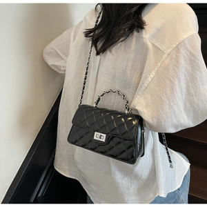 Detail of black quilted chain bag with metal turn-lock and leather shoulder strap