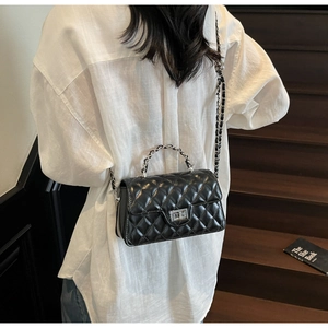 Detail of black quilted leather baguette bag with metal twist lock and chain strap