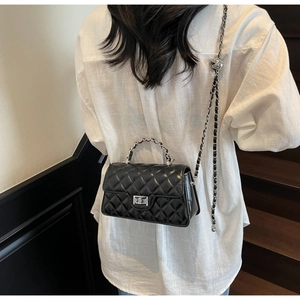 Rear view of model wearing a black quilted baguette bag with silver chain strap