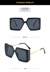 Detail of square oversized black and grey sunglasses with gold metal temples and carbon texture