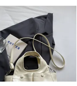 Detailed top view of a cream leather handbag with two front buckles on grey suit background