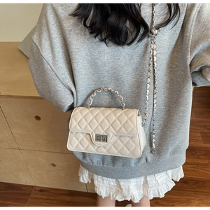 Close-up of beige quilted crossbody bag with silver chain strap on a model outfit