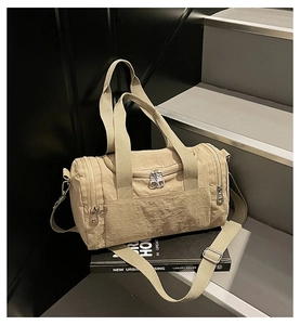 Detailed view of light beige nylon cylinder bag with multi-zipper pockets on urban books