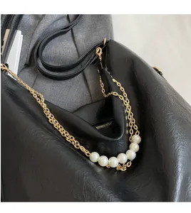 Close-up of black leather tote bag featuring gold hardware chain and white pearl accents