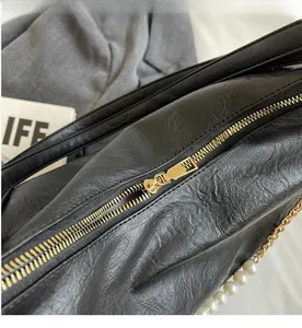 Detailed close-up of smooth gold zipper and white pearl strap on black leather bag