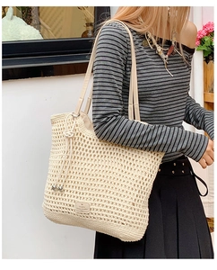 Detail of woven straw tote bag featuring leather shoulder strap and a side drawstring