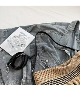 Dettaglio della borsa tote in paglia intrecciata con strisce nere e tracolla in pelle