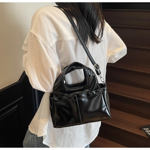 Detail of black glossy PU leather handbag with dual front pockets and adjustable strap