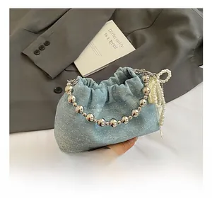 Detail of light blue denim drawstring bag with silver bead handle and pearl bow charm