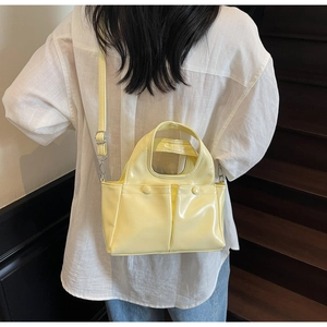 Detail of light yellow glossy bucket bag with front pockets on a person on stairs