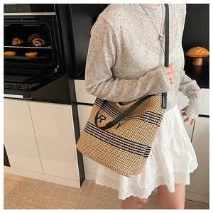 Détail d'un sac cabas en paille tissée avec rayures noires et lettre R imprimée