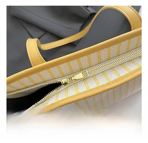 Detail of gold metal zipper and yellow leather trim on striped canvas tote bag