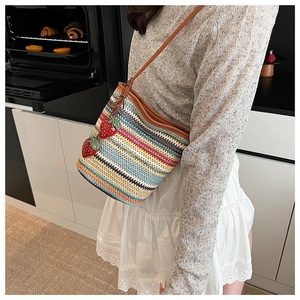 Détail d'un sac seau en paille tressée colorée avec des breloques fraises et bandoulière