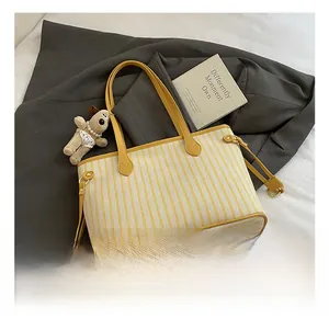 Detail view of yellow striped canvas tote with leather handles and plush charm