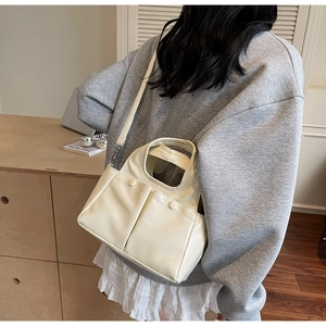 Model wearing a cream shoulder bag with dual front pockets in a cozy interior setting