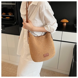 Detail of khaki woven bucket bag with leather strap and logo patch in a home setting