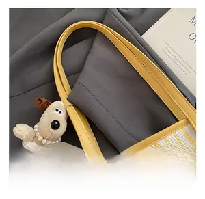 Detail of canvas tote bag with yellow leather handle and a cute cartoon dog plush charm