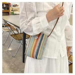 Close-up of a colorful striped woven crossbody bag with brown strap and button detail