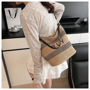 Détail du sac cabas en paille avec rayures noires et bandoulière en cuir sur table