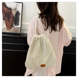 Detail of white crochet knit drawstring bucket bag with brown leather logo patch