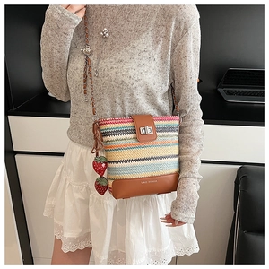 Rainbow striped straw bucket bag with strawberry charms and chain strap on female model