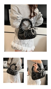 Détail du sac à main plissé en cuir verni noir avec un nœud en perles blanches et anse à volants