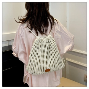 Detail of white knit drawstring backpack featuring floral crochet mesh and leather tag