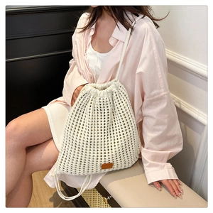 Close-up of cream knit drawstring bucket bag featuring hollow floral pattern and leather patch