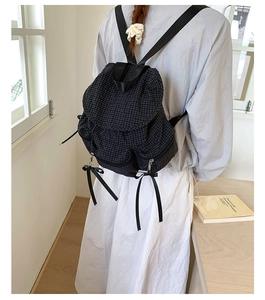 Détail d'un sac à dos en toile à carreaux noirs avec des nœuds décoratifs en ruban