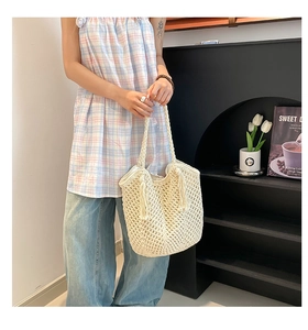 Detail of a beige hollow-out woven tote bag with tassels on a lifestyle background