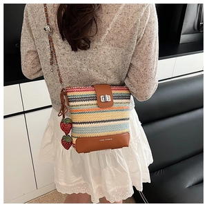 Detail of colorful woven bucket bag with metal lock and strawberry charms on model
