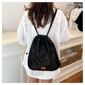 Detail of black crochet drawstring backpack with mesh texture and brown leather label