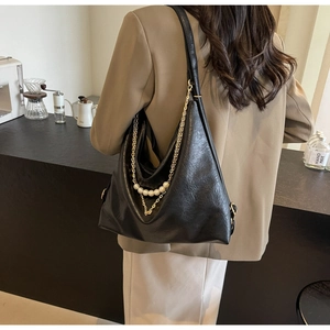 Close-up of black leather tote with gold chain and white pearl pendant charm