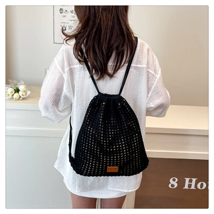 Detail showing black crochet knit drawstring backpack with hollow floral patterns and leather tag