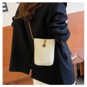Detail of a beige woven mini crossbody bag featuring a round wooden button closure