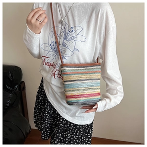 Détail d'un sac seau en paille à rayures arc-en-ciel avec bandoulière en cuir brun