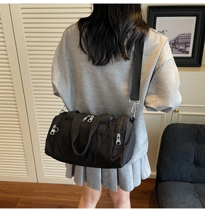 Rear view of model wearing a black nylon barrel bag with silver zippers and wide strap
