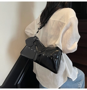Rear view of a black glossy patent leather shoulder bag with silver studs and heart charm