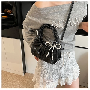 Détail du sac froncé en cuir verni noir avec charm nœud en perles et bandoulière amovible