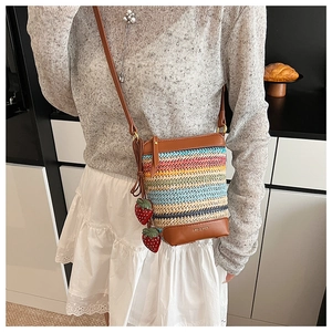 Detail of colorful woven straw crossbody bag with leather trim and strawberry charms