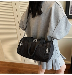 Detailed back view of a black nylon barrel bag shown on a model for size and scale