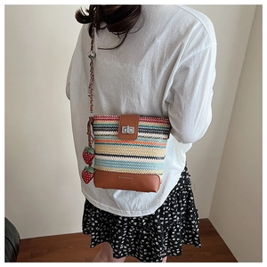 Detail of colorful striped straw bucket bag with strawberry charms and metal chain strap
