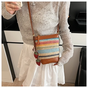 Detail of colorful rainbow straw crossbody bag with red strawberry charms and leather base