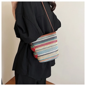 Vue détaillée du sac seau en paille tissée à rayures colorées et breloque fraise
