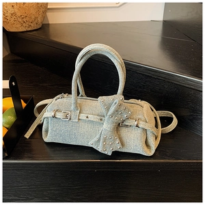 Detailed view of blue denim baguette bag with large bow and silver studs on black stairs