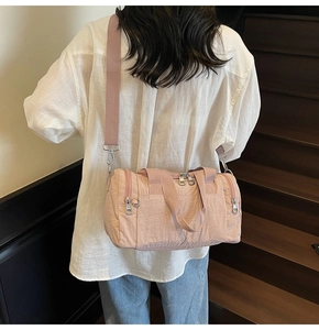 Lifestyle view of a pink nylon barrel bag with wide strap on a person's shoulder