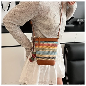 Detail of rainbow straw woven crossbody bag with brown leather trim and strawberry charms